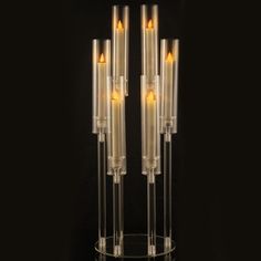 three tall clear candles with yellow lights in them on a glass stand against a black background