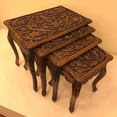 three carved wooden tables sitting on top of a white tablecloth covered countertop in front of a beige wall