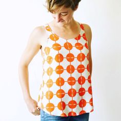 a woman standing in front of a white wall wearing a tank top with orange circles on it