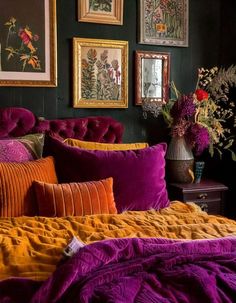 a bed covered in purple and orange pillows next to pictures on the wall above it