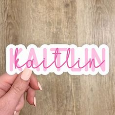 a person holding up a sticker that says kastillinn in pink lettering