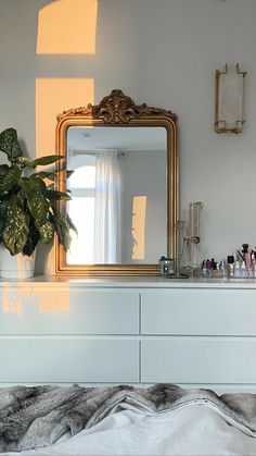 a white dresser topped with a mirror next to a potted plant