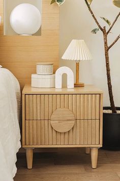 a nightstand with a lamp on top of it next to a bed and a tree