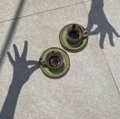 two cups of coffee sitting on top of a cement floor next to a shadow of a person's hand