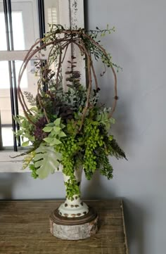 a vase filled with lots of green plants on top of a wooden table next to a mirror