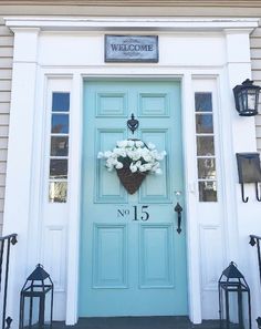 a blue front door with white flowers on it and a welcome sign above the door