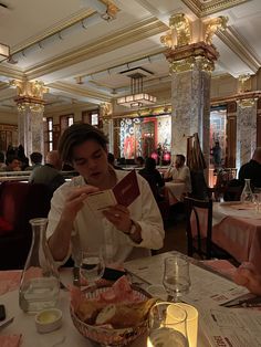 a man sitting at a table with a book in his hand and wine glasses on the table