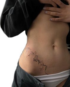 a woman's stomach with a small tattoo on the side and her hands behind her back