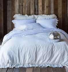 the bed is made with white linens and ruffled pillows on top of it