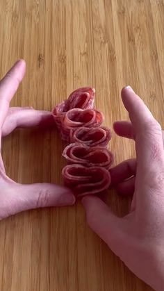 two hands are holding small pieces of food on a wooden surface, while another person holds out their hand to the camera