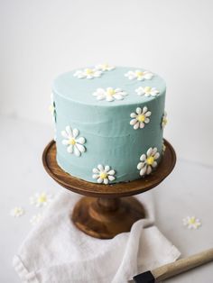 a blue cake sitting on top of a wooden stand next to a white napkin and spatula