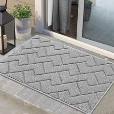 a gray door mat sitting on top of a stone floor next to a potted plant