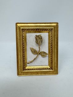 a gold framed photo with a single rose in it's center, on a white background