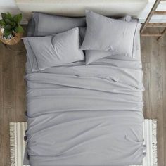 an overhead view of a bed with grey sheets and pillows on top of wooden flooring