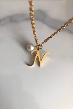 "Letter N necklace, set on a stainless steel ,golden color chain. Chain length 19'  With addition cost there is an option to add a white freshwater pearl, as a charm, next to the letter. 6 mm, white round pearl Kindly choose your option. Beautiful spiritual gift. Please make sure you to pay attention to the size of the pendant. I have added pictures next to 25 cent coin, and measurement tape.  Need a different length just write it to me in the \"message to the seller\" box of the order form. **L N Letter Necklace, Elegant Stainless Steel Initial Pendant Necklace, Gold Minimalist Initial Necklace In Stainless Steel, Minimalist Gold Stainless Steel Initial Necklace, Elegant Initials Necklace In Stainless Steel, Elegant Initials Stainless Steel Necklace, Elegant Stainless Steel Initials Necklace, Personalized Pearl Necklace With Initial Pendant As Gift, Initial Pendant Necklace With Pearl For Gift