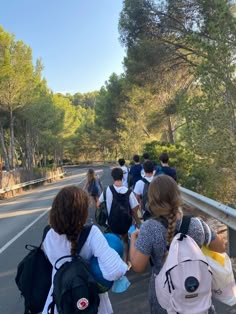 a group of people walking on the side of a road with backpacks over their shoulders