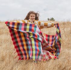 a woman is standing in the middle of a field holding a plaid blanket