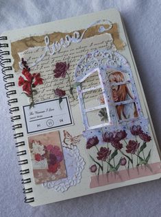 an open notebook with altered images and flowers on the cover, sitting on a bed sheet