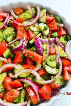 cucumber, onion and tomato salad in a white bowl on top of a table