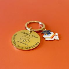 a gold keychain with a graduation cap and diploma on it sitting on an orange surface