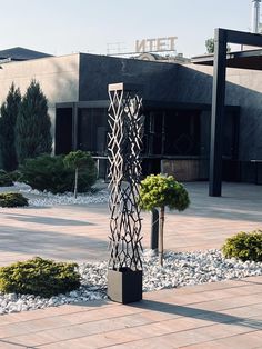 a tall metal sculpture sitting in the middle of a garden next to a parking lot