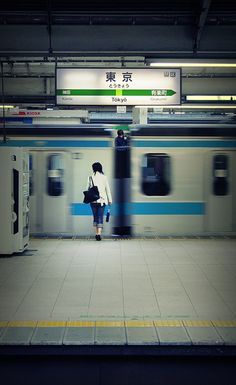 a woman standing in front of a train at a subway station with her back to the camera