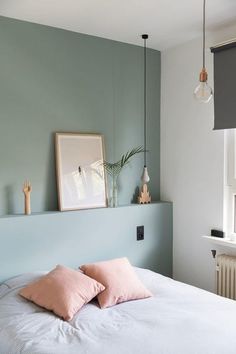 a bed with two pink pillows on top of it next to a wall mounted light