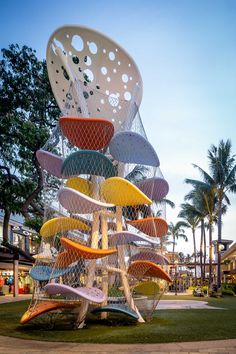 a large sculpture made out of many different colored chairs on the grass in front of palm trees