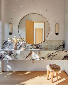 a bathroom with marble counter tops and a round mirror on the wall, along with stools