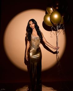 a woman in a gold dress holding balloons and posing for the camera with her hands behind her back