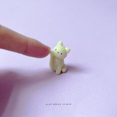 a tiny toy bear sitting on top of a white paper next to a finger touching it