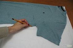 a person is holding a pencil and drawing on a t - shirt that has been folded down