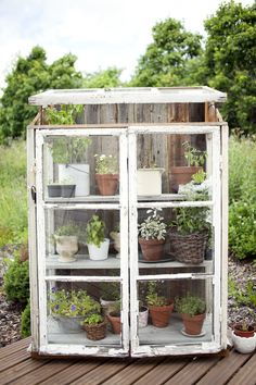 an old cabinet filled with potted plants on top of a wooden deck in front of some bushes