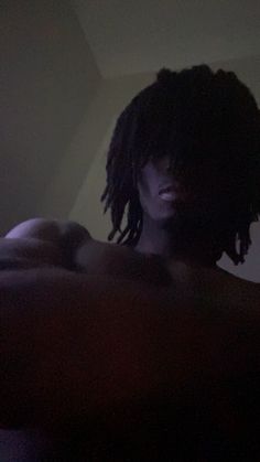 a person with dreadlocks laying on a bed in the dark and looking off to the side