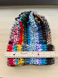 a multicolored crocheted beanie sits next to a ruler