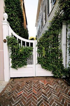 an open white gate with ivy growing on it's sides in front of a building