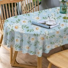 a blue table cloth with white daisies and green leaves on it next to a wooden chair