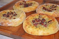 four small pizzas sitting on top of a wooden cutting board