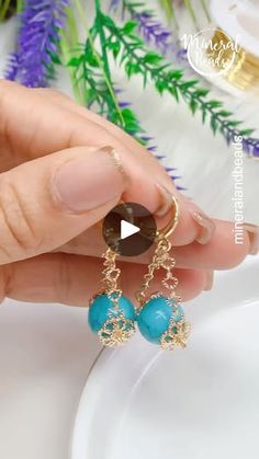 the woman is holding her earrings with blue beads and gold chains on it's ear