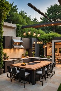 an outdoor kitchen and dining area with lights hanging from the ceiling, surrounded by greenery