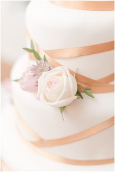 a close up of a wedding cake with flowers on the top and ribbons around it