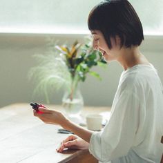 a woman sitting at a table with a remote control in her hand and looking at the screen