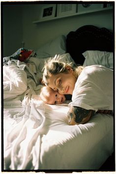 a woman laying in bed next to a man with tattoos on his arms and chest