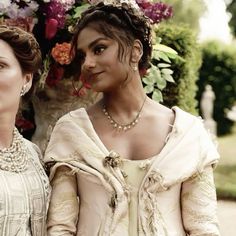 two women standing next to each other in front of flowers