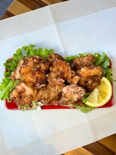 a red plate topped with chicken and lettuce next to a slice of lemon