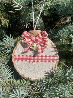 a christmas ornament hanging from a pine tree with red and white plaid ribbon