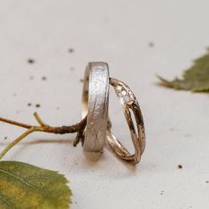 two wedding rings sitting next to each other on top of a white surface with leaves