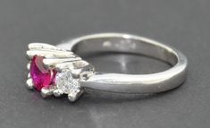 This is a very fine grade Ruby Ring. It is crafted from solid thick Platinum. The ring hold three stones. The center being a very fine grade natural untreated Ruby. It is a round cut and set very securely with four raised prongs. The ruby is of fabulous quality no visible inclusions or abrasions. The color is a deep red with a pink hue. The first two photographs are in natural morning light. The fine stone changes color under different light as you can see from the photographs. On either side of Formal Ruby Three Stone Ring With Diamonds, Luxury Three Stone Ruby Ring For Wedding, Classic Three Stone Round Ruby Ring, Round Ruby Ring In Platinum For Wedding, Classic Three Stone Ruby Ring With Diamonds, 14k White Gold Ruby Ring With Brilliant Cut, Oval Ruby Ring With Three Diamonds, Oval Three Stone Ruby Ring With Diamonds, Elegant Three Stone Ruby Ring