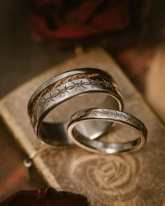 two silver rings with the names of different people engraved on them sitting next to an open book