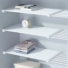 three white shelving shelves with books, shirts and a clock on top each shelf